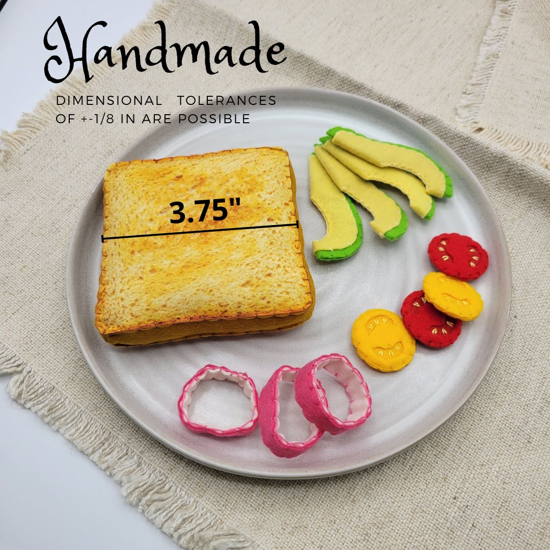 Plate with bread, avocado, tomato, and onion ring plush food toy on a textured surface.
