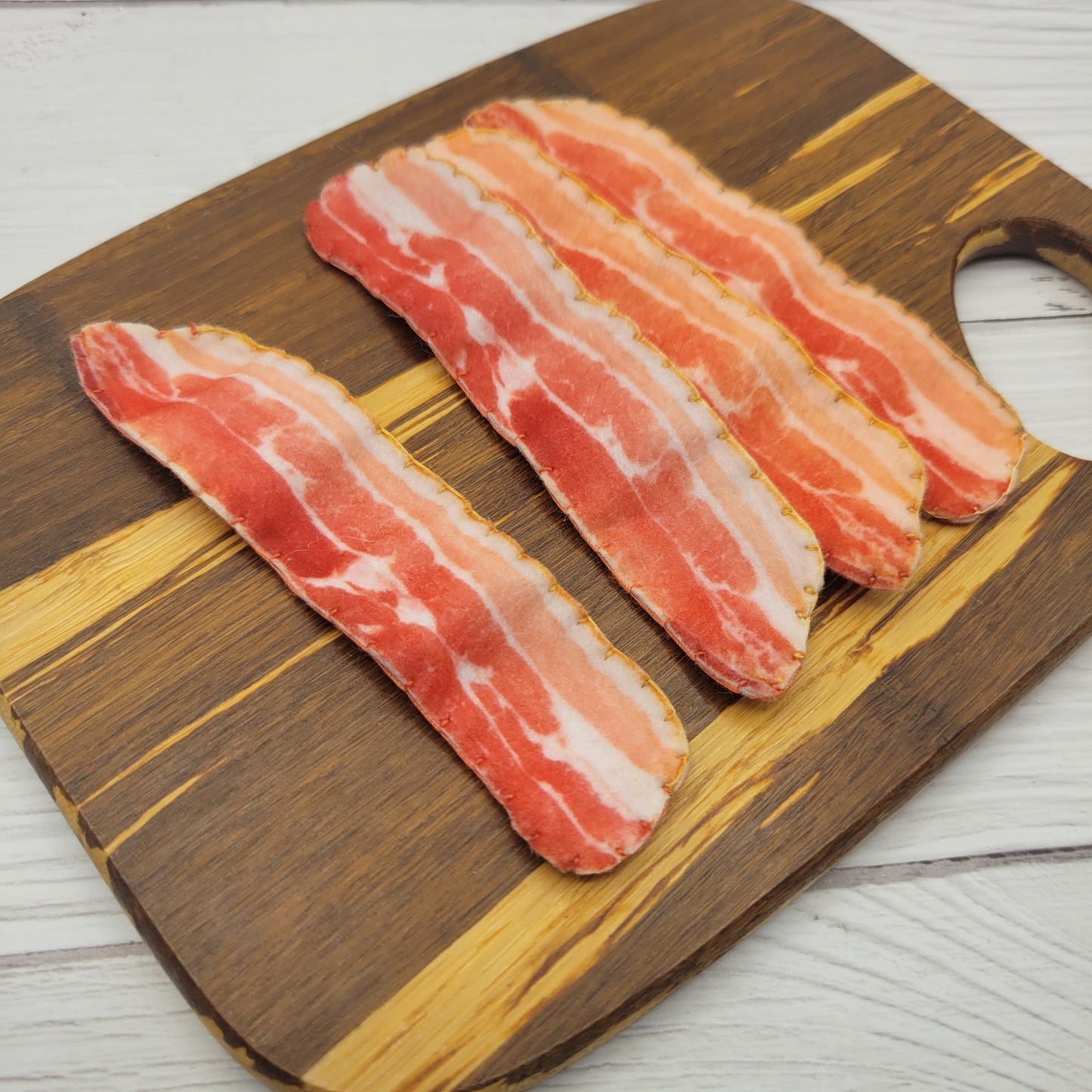 Three slices of raw pretend play plush bacon on a wooden cutting board.