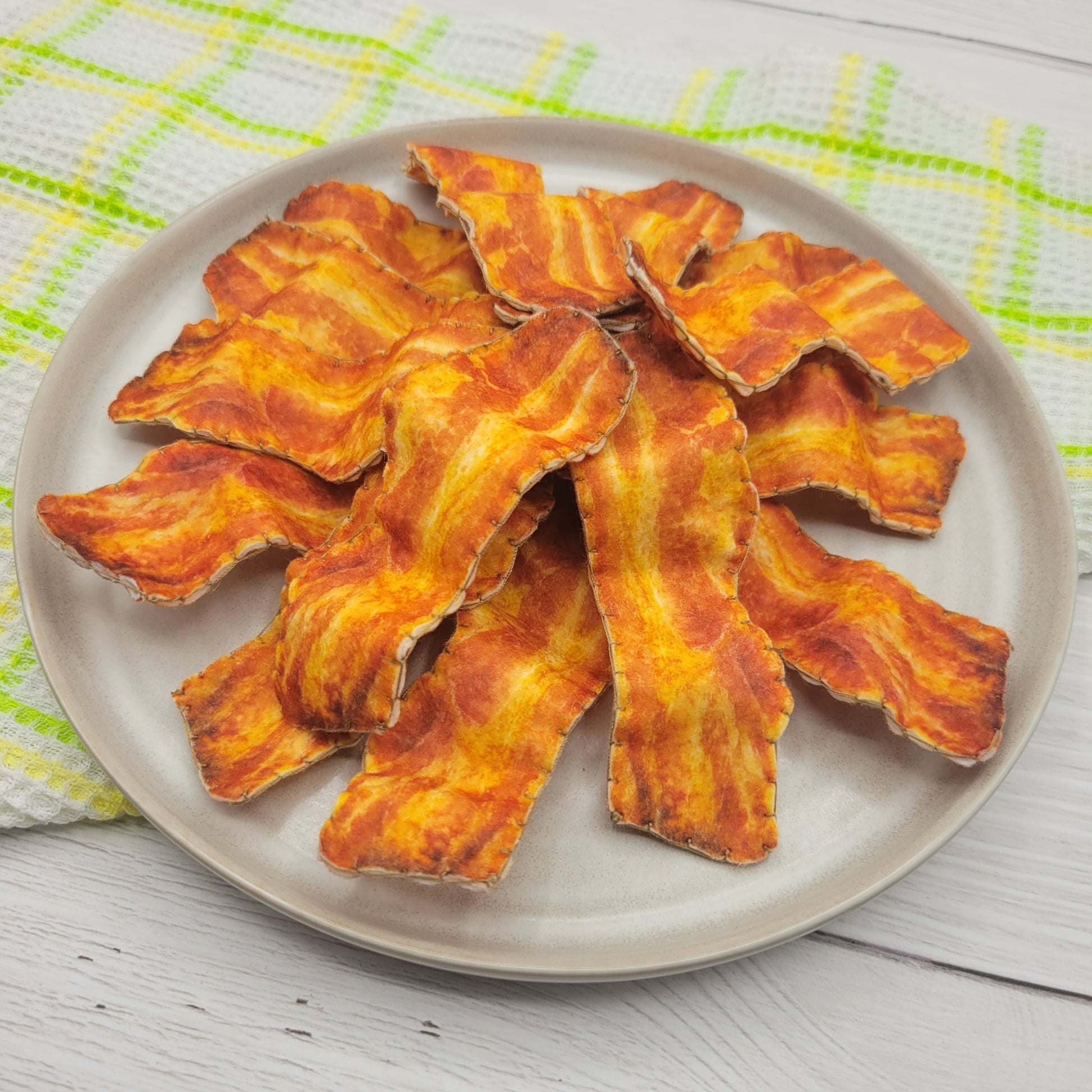 Bacon pretend play plush chips on a beige plate with a checkered cloth background
