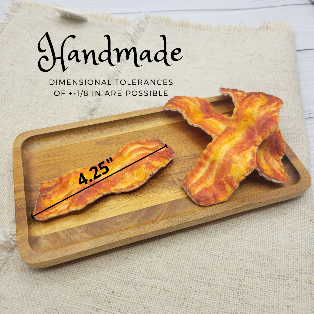 Wooden tray with bacon-shaped cutouts of plush food and measurement details on a textured surface.