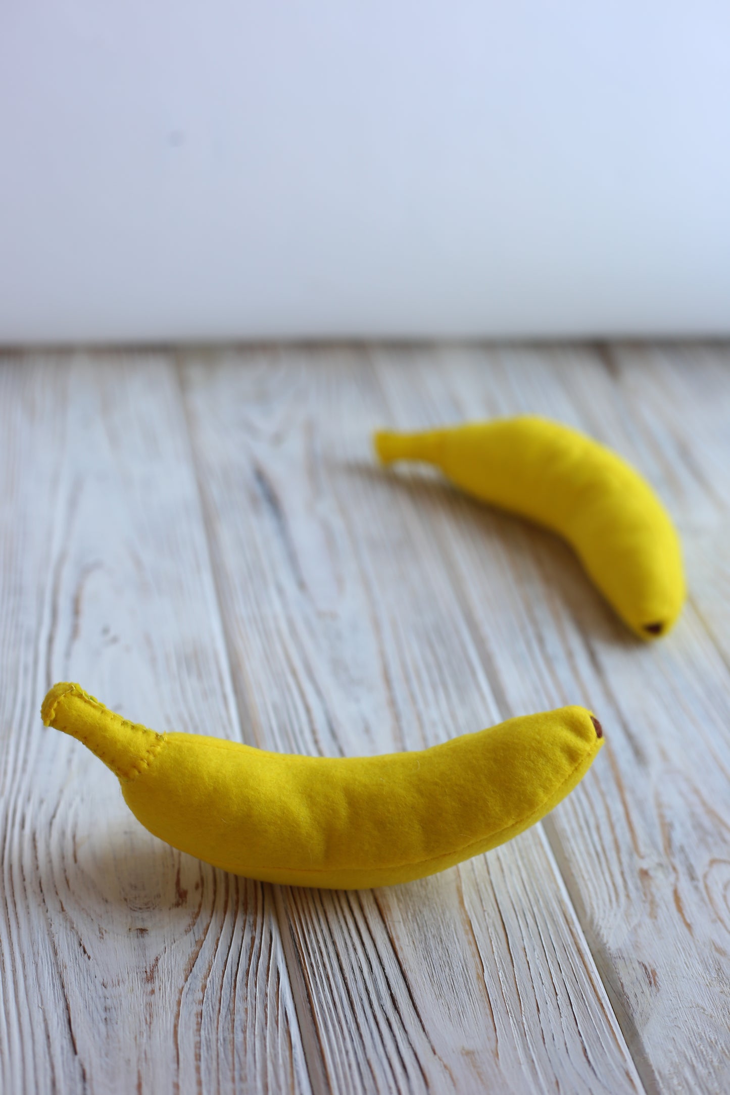 Two yellow banana plush food toys on a wooden surface.