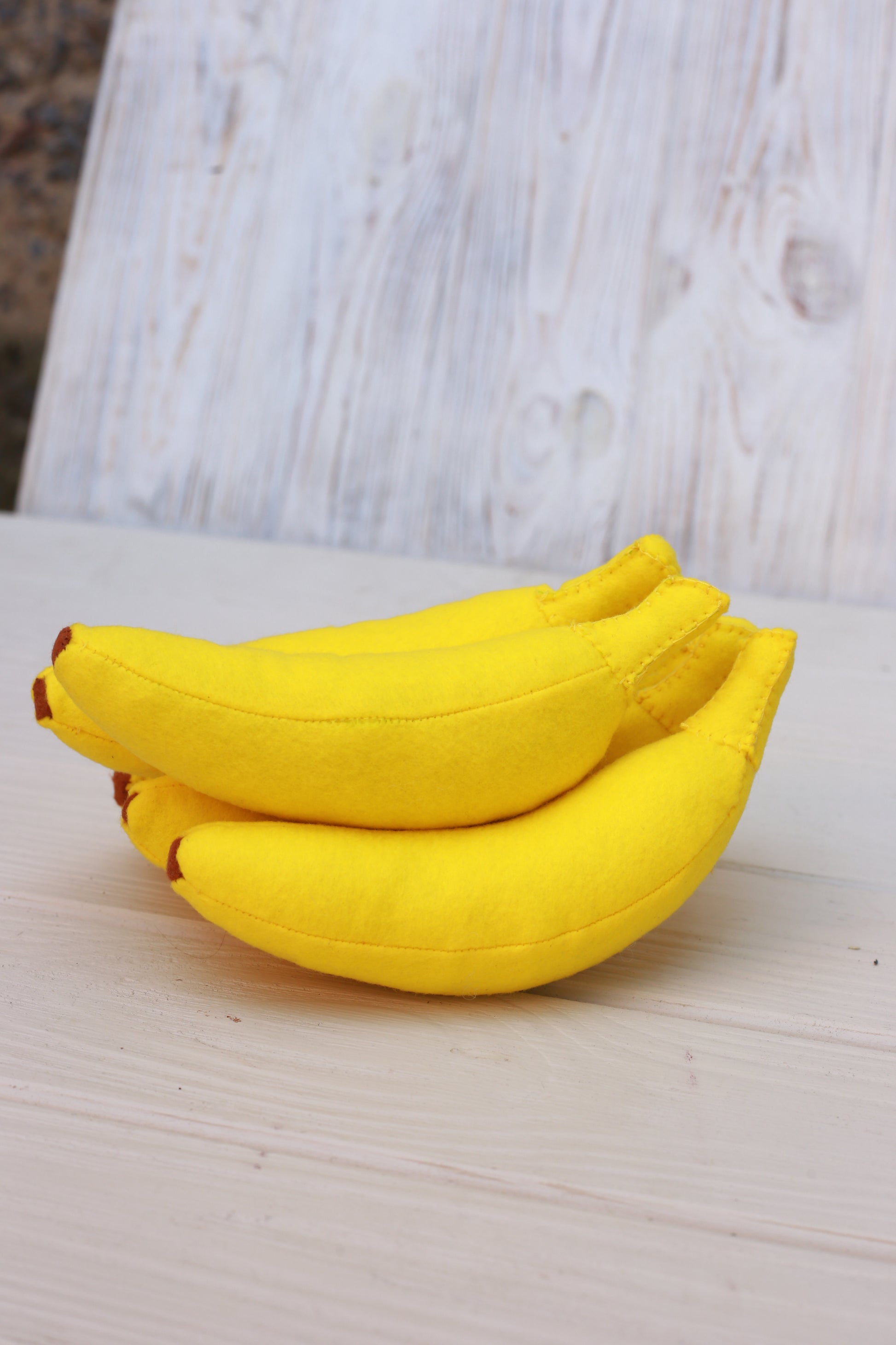 Three yellow bananas plush food toys on a light wooden surface