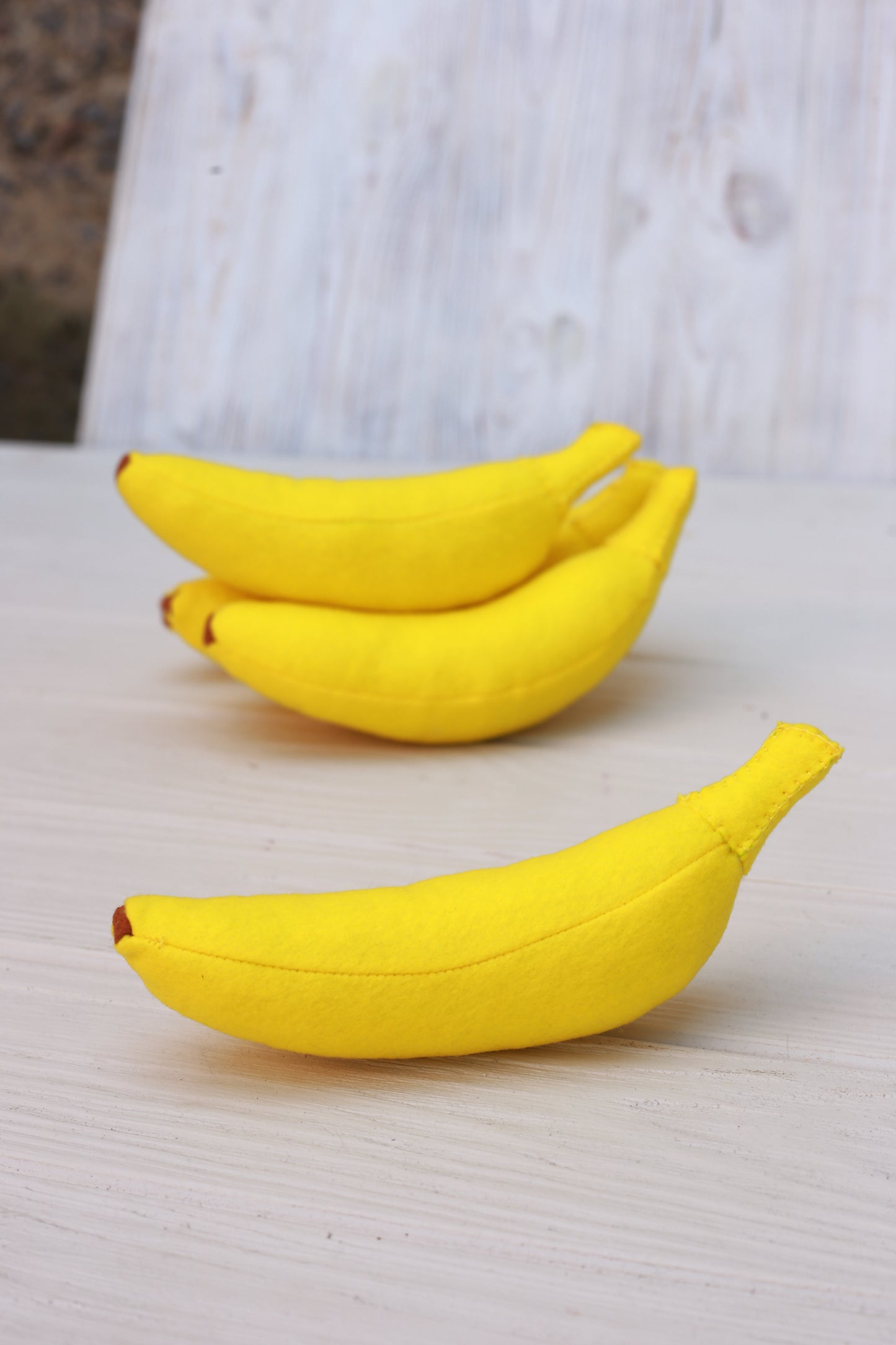 Two yellow banana plush food toys on a light wooden surface
