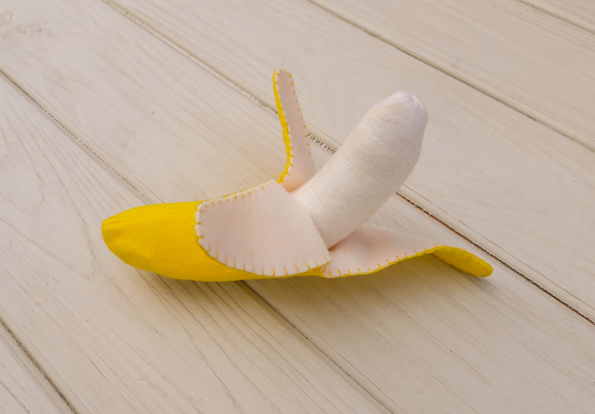 Yellow plush food toy banana with pink interior on a light wooden floor