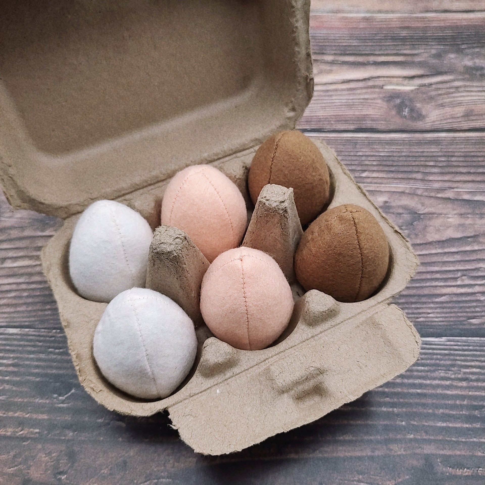 Egg-shaped pretend play toys in a cardboard box on a wooden surface