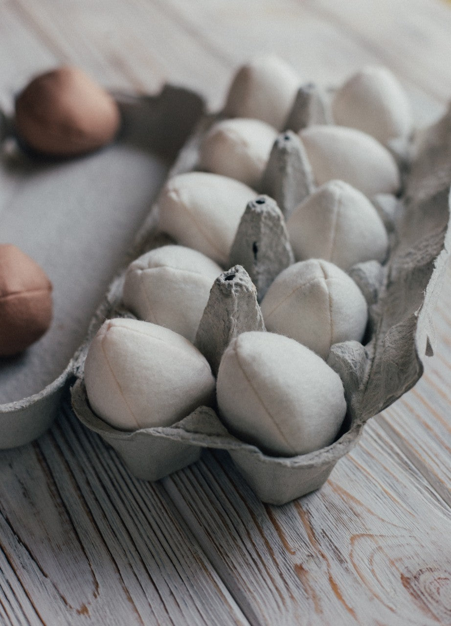 Felt eggs in a cardboard carton on a wooden surface
