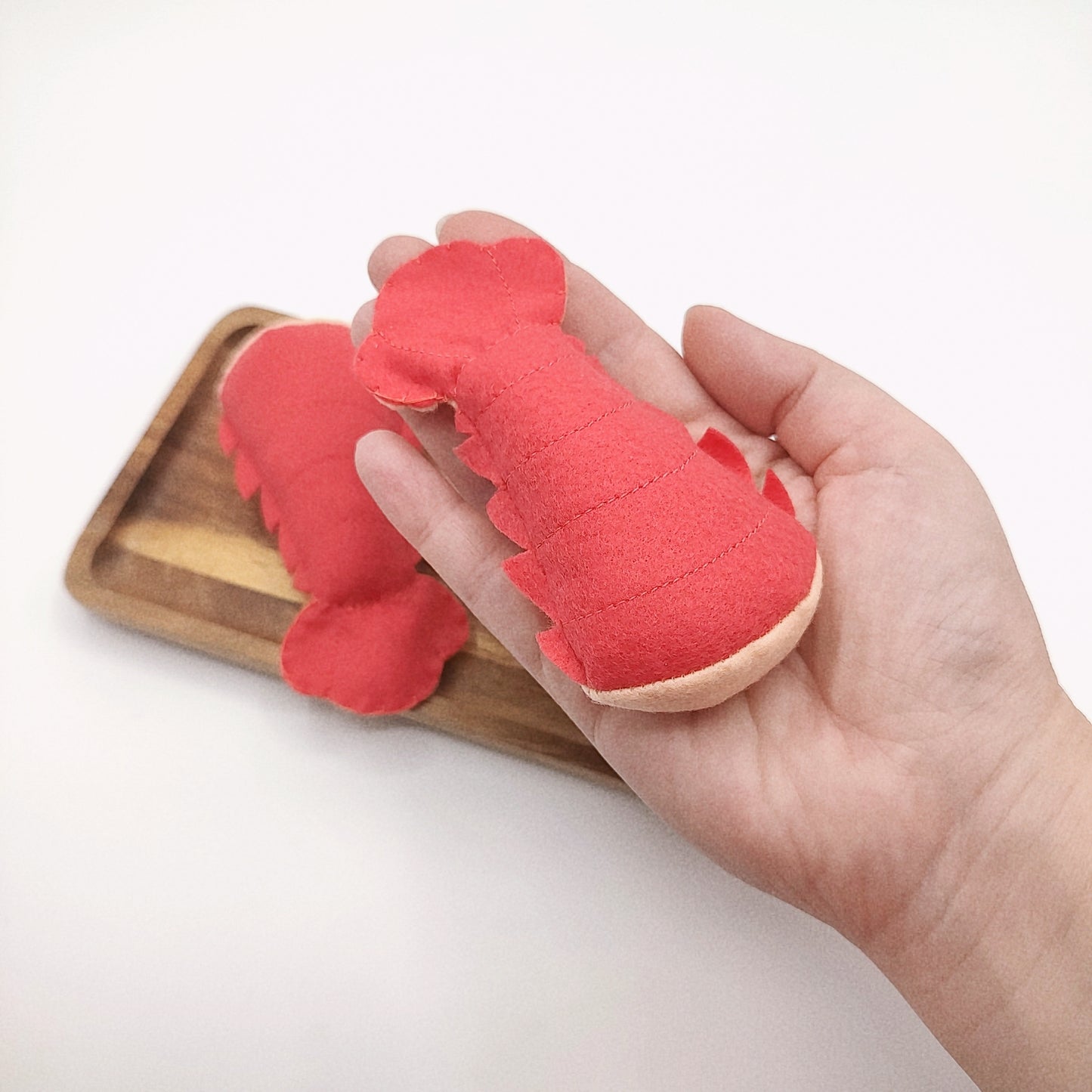 Red lobster-shaped toy held in a hand with a wooden tray in the background