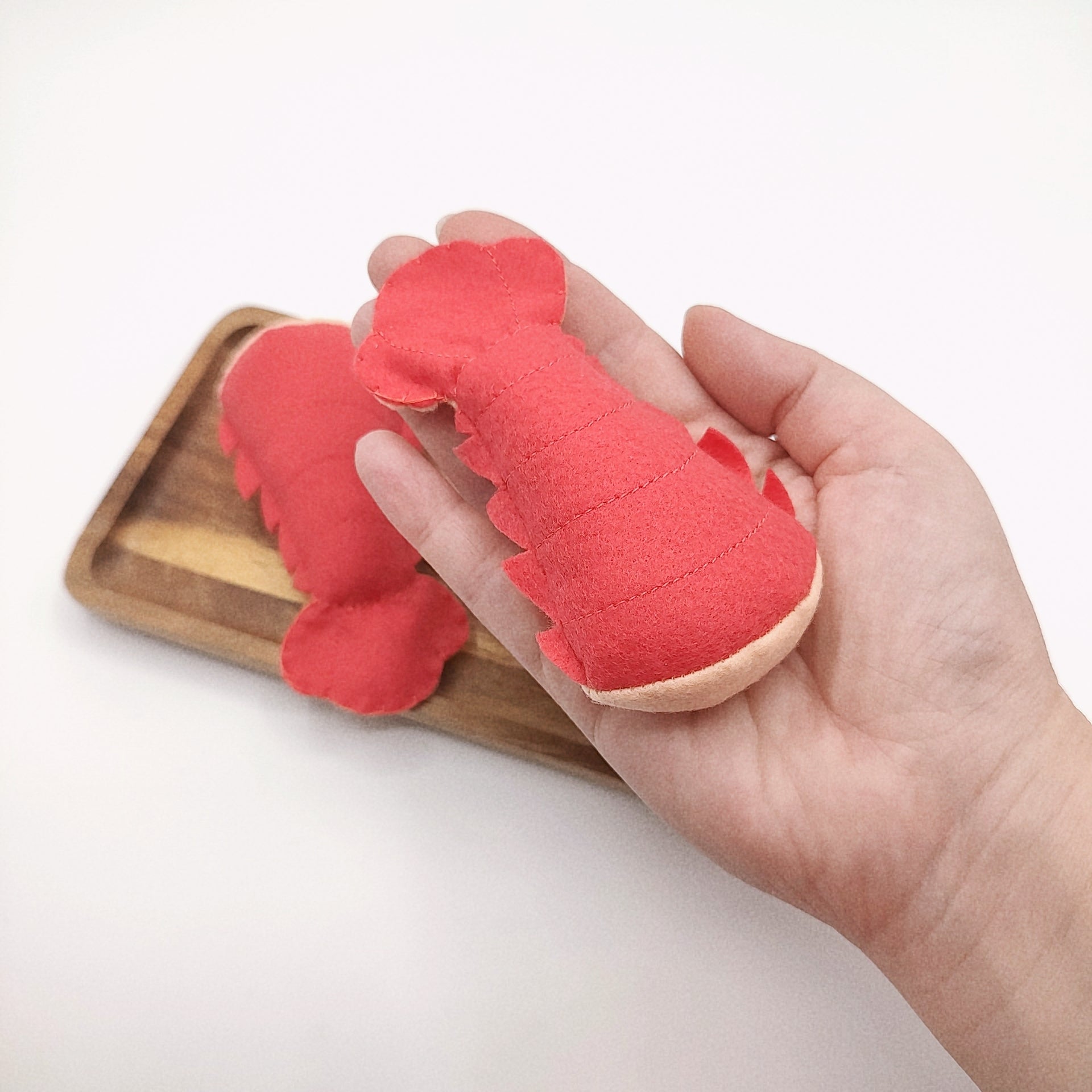 Red lobster-shaped toy held in a hand with a wooden tray in the background