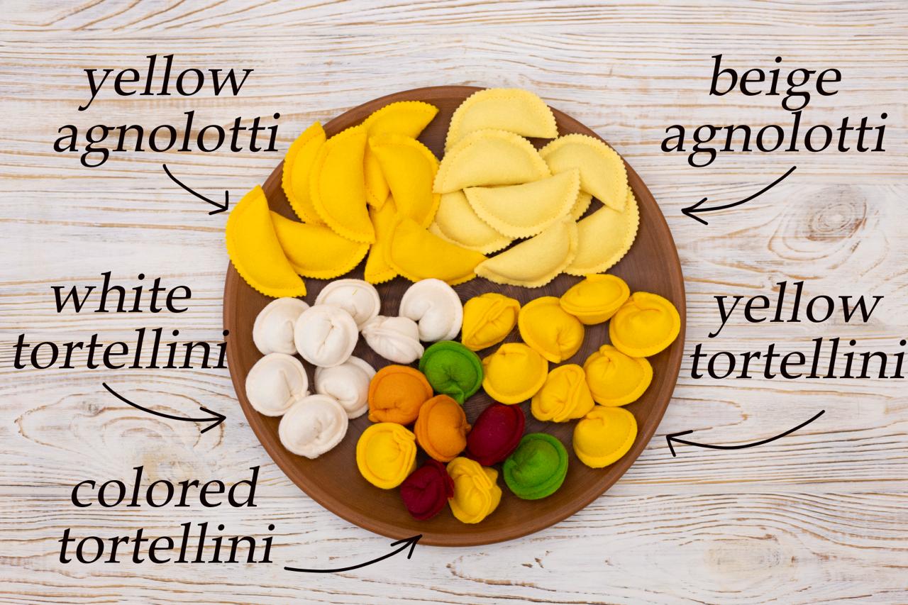 Wooden board with plush play yellow agnolotti, beige agnolotti, white tortellini, and colored tortellini on a wooden surface.