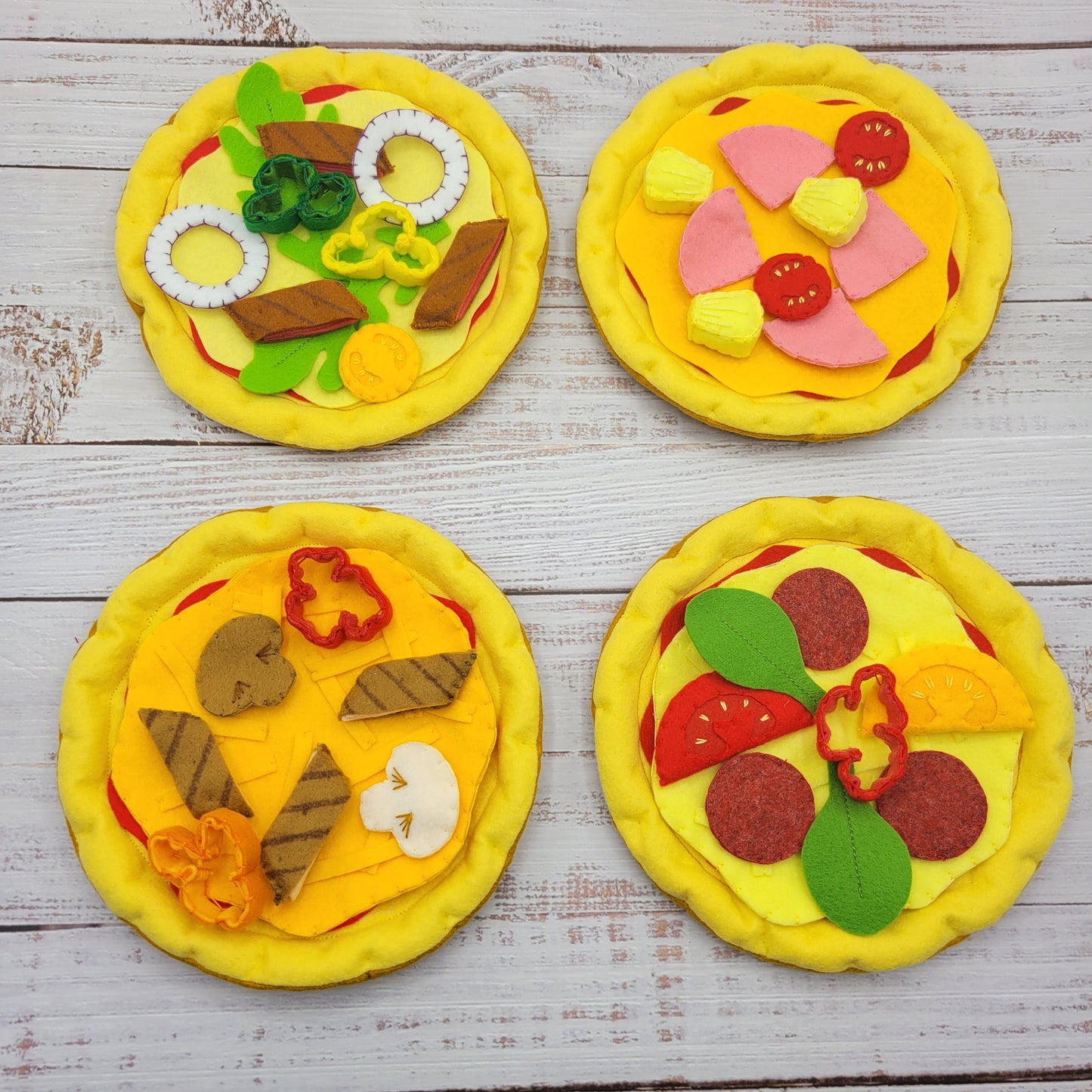 Four felt pizzas with various toppings on a wooden surface