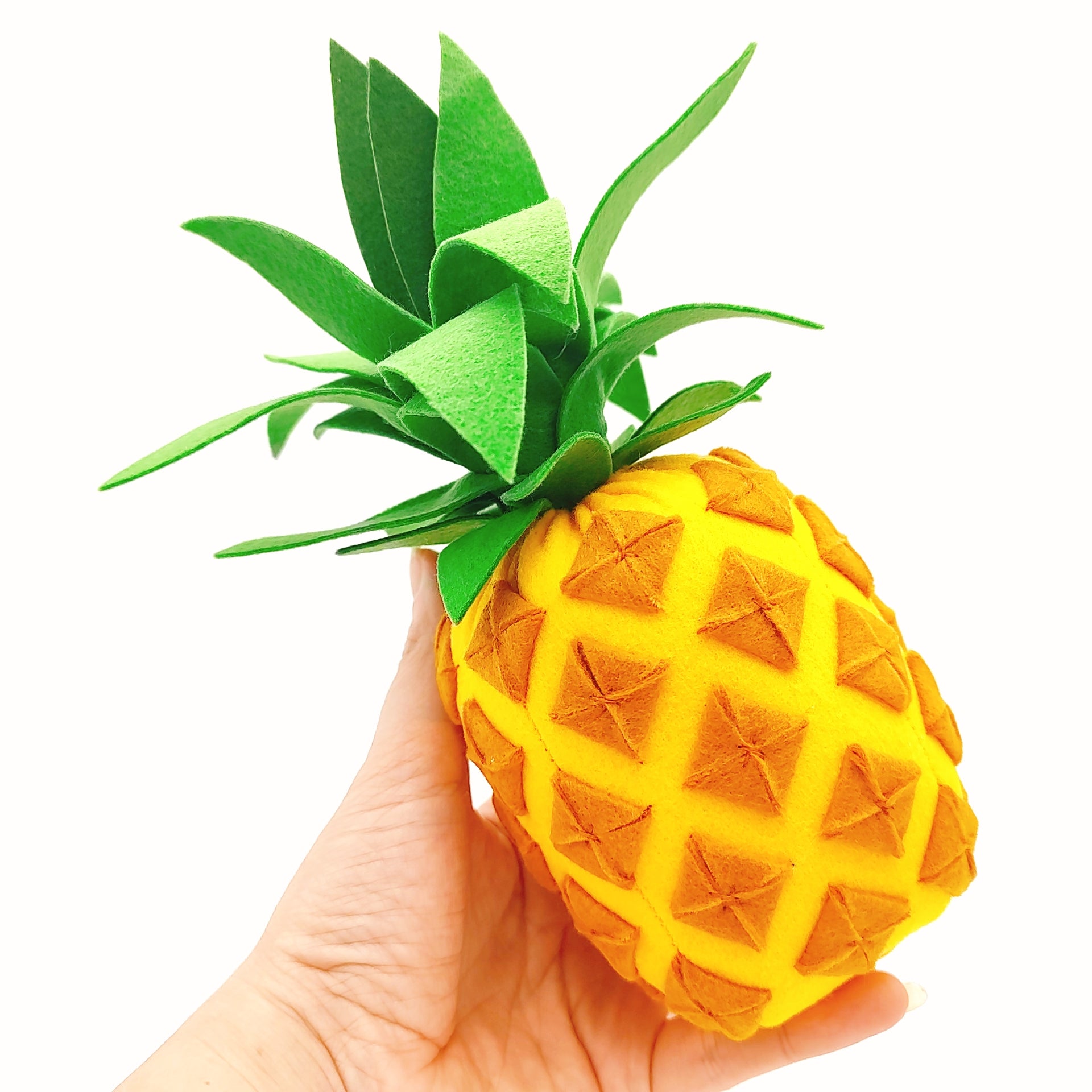 Hand holding a pineapple plush toy with green leaves on a white background
