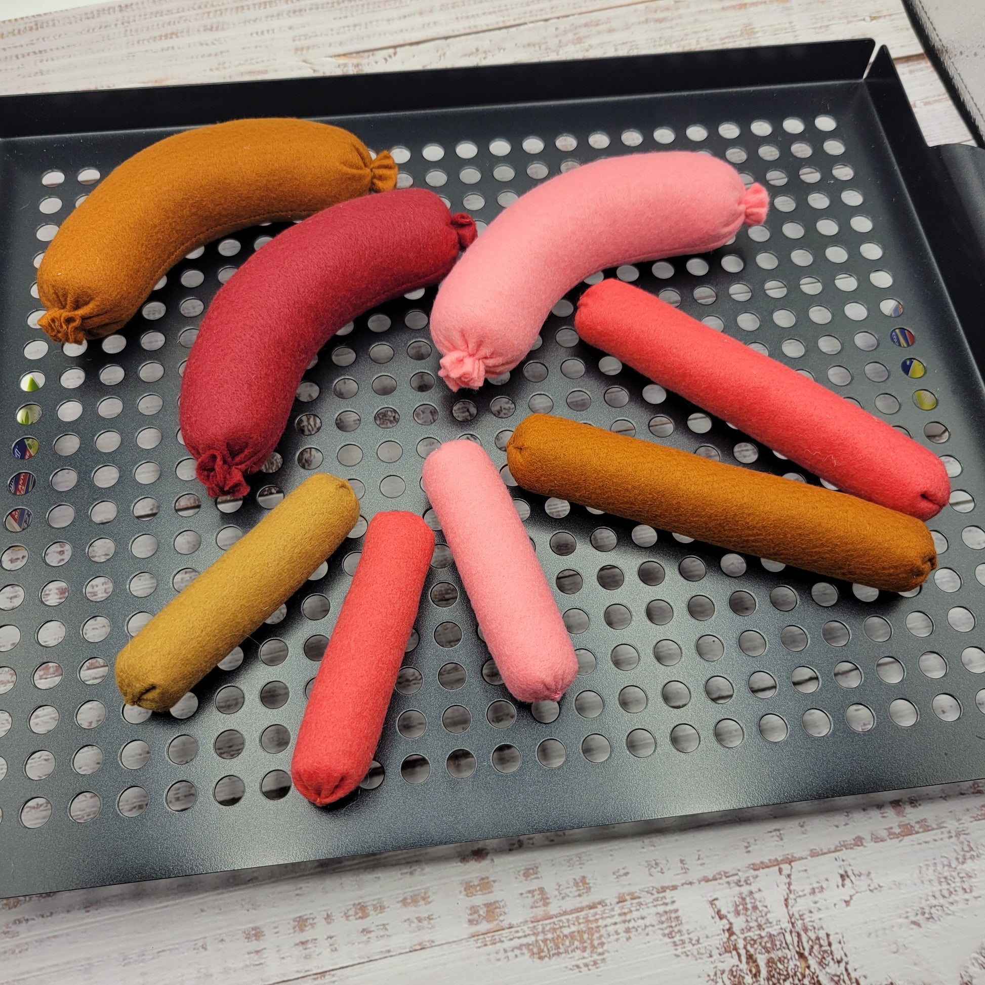 Colorful fabric sausages on a perforated metal tray.