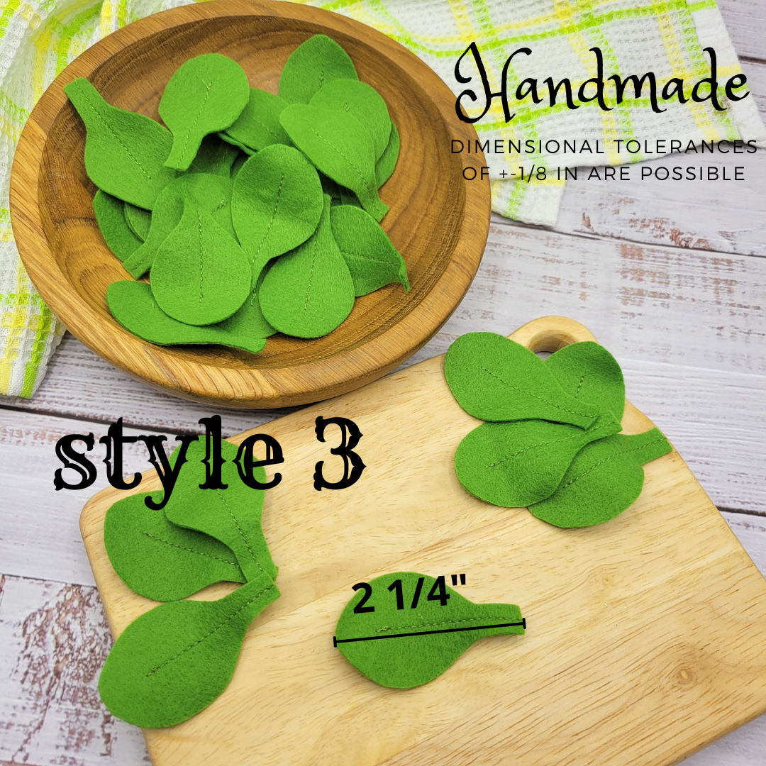 Green leaf-shaped salad plush food toy on a wooden board with a wooden bowl of additional cutouts, on a rustic wooden surface.