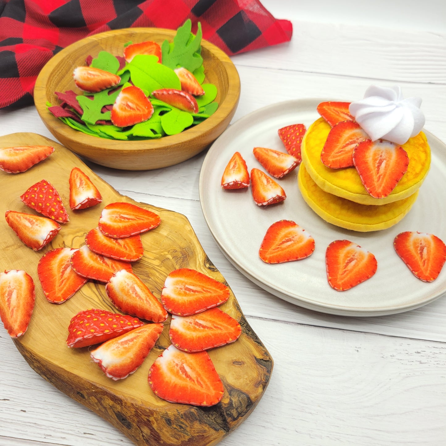 Fruit platter with sliced strawberries plush food toy on a wooden board and plate, on a white wooden surface.