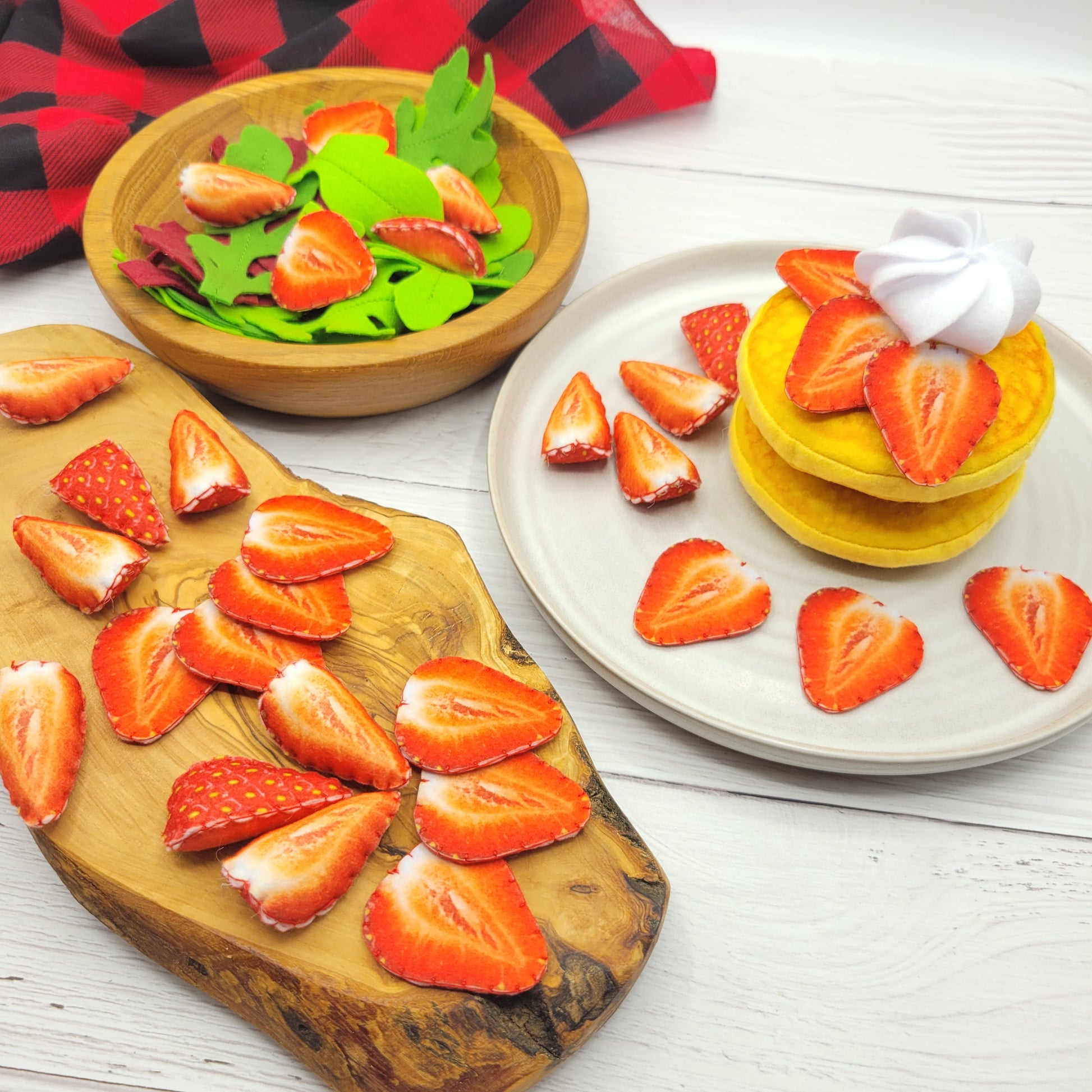Fruit platter with sliced strawberries plush food toy on a wooden board and plate, on a white wooden surface.