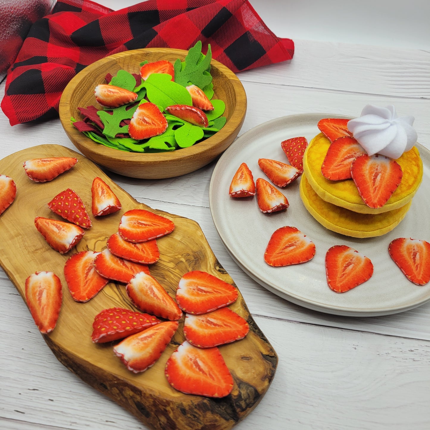 Strawberries plush food toy on a wooden board and plate with a red checkered towel.